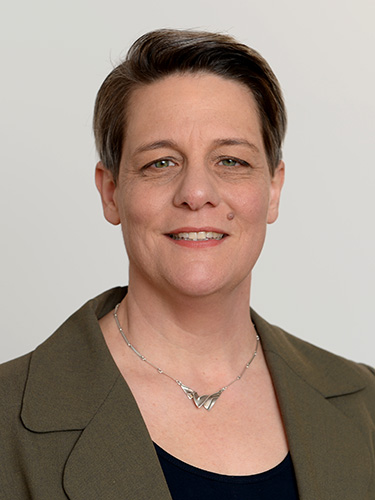 Porträt einer lächelnden Frau mit kurzem dunklem Haar, grauem Hintergrund und olivgrünem Blazer. Porträt einer lächelnden Frau mit kurzem dunklem Haar, grauem Hintergrund und olivgrünem Blazer.
