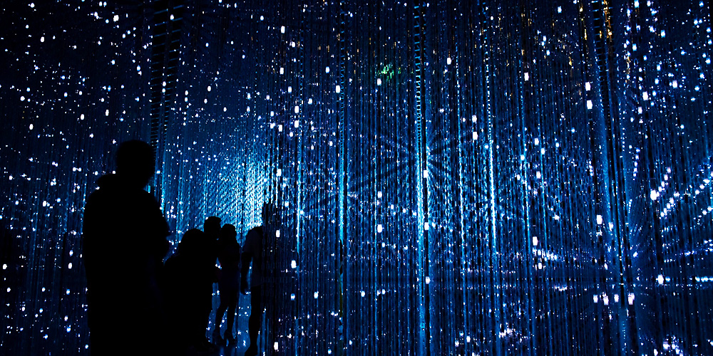 Menschen in dunklem Spiegellabyrinth mit Dutzenden Reflektionen von Handybildschirmen