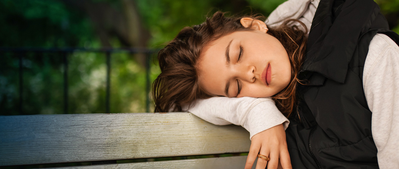 Tired woman sleeping on wooden bench outdoors.