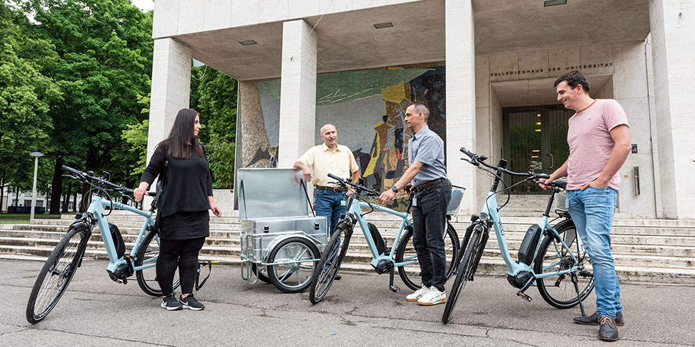 Several people with e-bikes and a bike trailer in front of the entrance to the Kollegienhaus