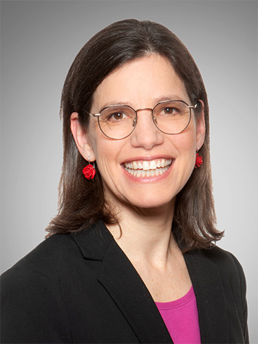 Porträt einer lächelnden Frau mit schulterlangem braunem Haar, Brille, roten Ohrringen, schwarzem Blazer und pinkem Oberteil. Porträt einer lächelnden Frau mit schulterlangem braunem Haar, Brille, roten Ohrringen, schwarzem Blazer und pinkem Oberteil.