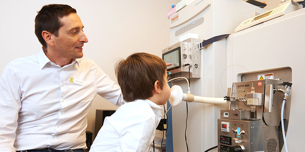 Prof. Dr. Pablo Sinues sits next to a boy blowing into a machine.