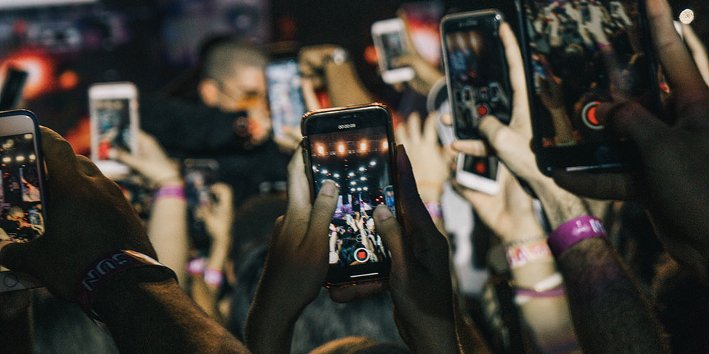 Numerous hands with smartphone, filming a concert.