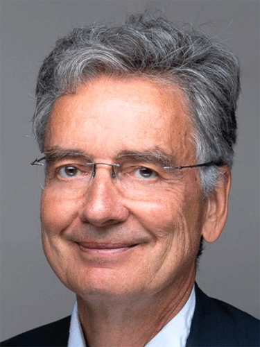Portrait of an older man with gray hair, wearing glasses and a dark suit jacket over a white shirt, smiling slightly against a plain gray background. Portrait of an older man with gray hair, wearing glasses and a dark suit jacket over a white shirt, smiling slightly against a plain gray background.