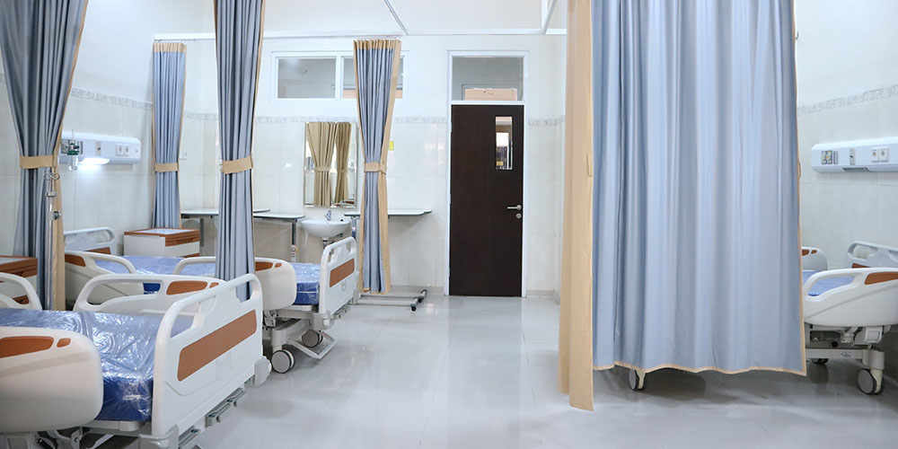 A bright room in a hospital, in the middle a door leads outside, to the left and right of it are empty hospital beds. 