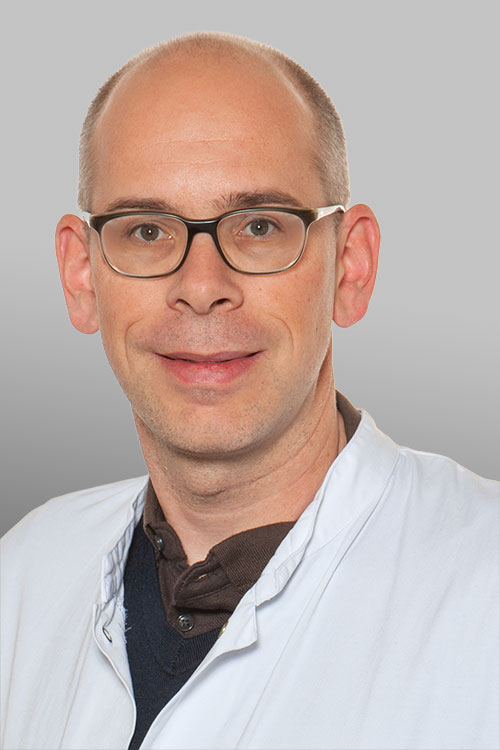Portrait of Gregor Hutter wearing a white coat against a gray background. Portrait of Gregor Hutter wearing a white coat against a gray background.