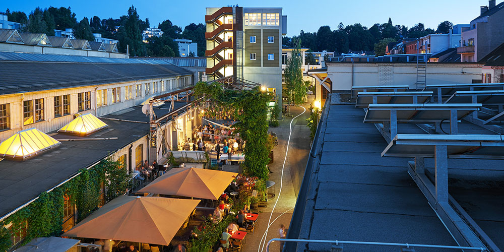 Blick von oben auf die Aussenterasse eines Restaurants und weitere Gebäude des Gundeldinger Felds.
