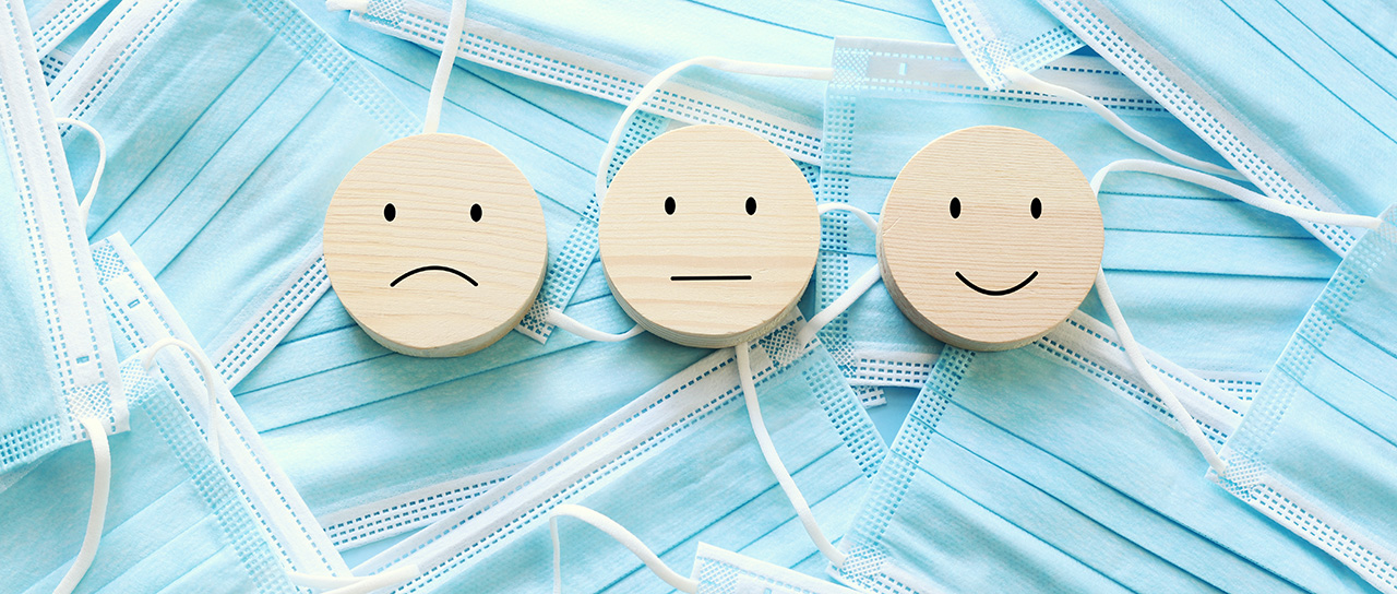 Drei Smilies mit unterschiedlichem Gesichtsausdruck vor einem Hintergrund aus Hygienemasken