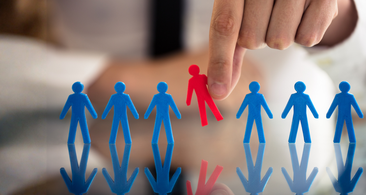 Eine Hand nimmt aus einer Reige blauer Figuren die einzige rote Figur heraus.