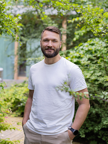 Florian Knappe wearing a white t-shirt, with trees in the background Florian Knappe wearing a white t-shirt, with trees in the background