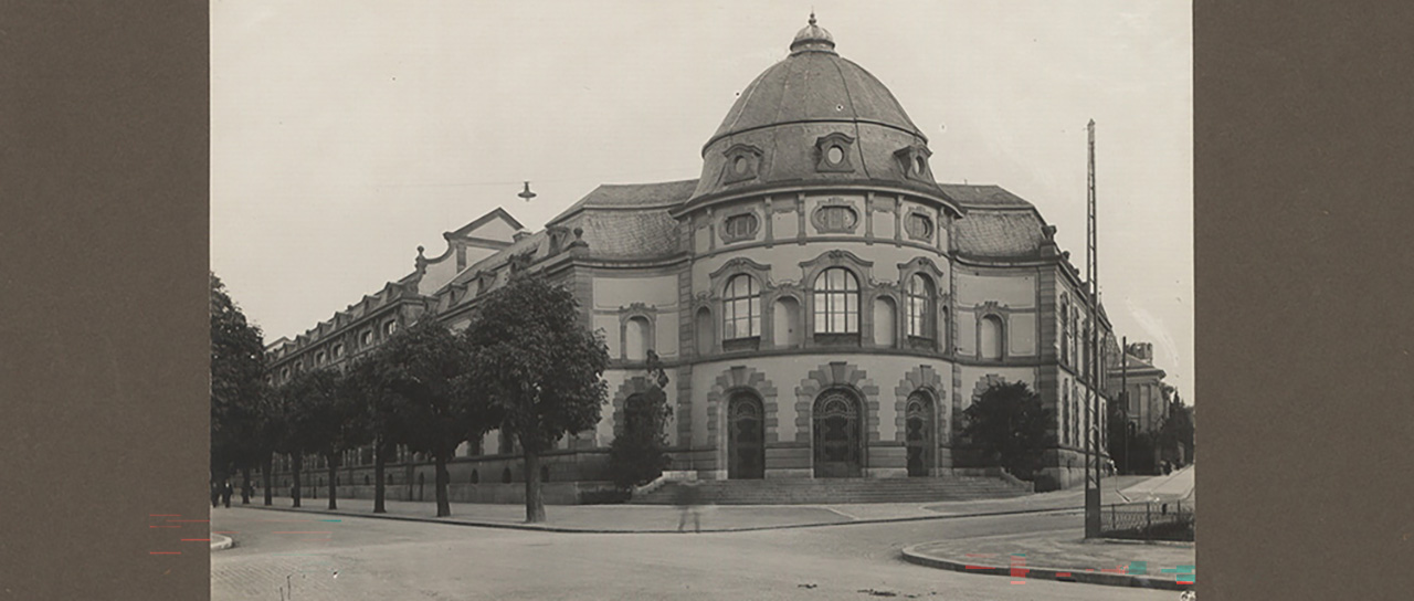 Historical black-and-white photograph of a grand building with a domed roof and ornate façade on a quiet street corner.