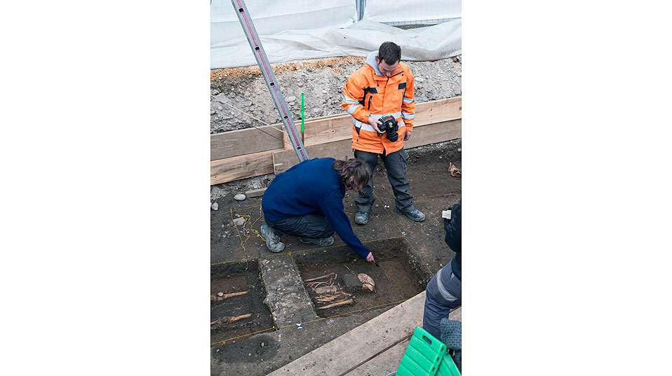 Archäologen dokumentieren eine Grabgrube, die sich im helleren Kies abzeichnet. (Foto: Universität Basel, Roland Schmid)