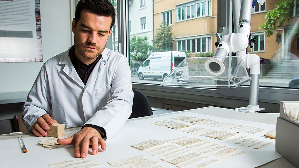 Projektmitarbeiter Gabriel Schaffter reinigt die Zettel einzeln mit einem Schwamm und einem Absauggebläse. (Bild: Universität Basel, Florian Moritz)