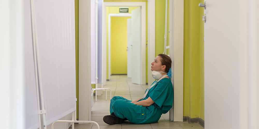 Müde Pflegerin sitzt in einem leeren Gang am Boden. 