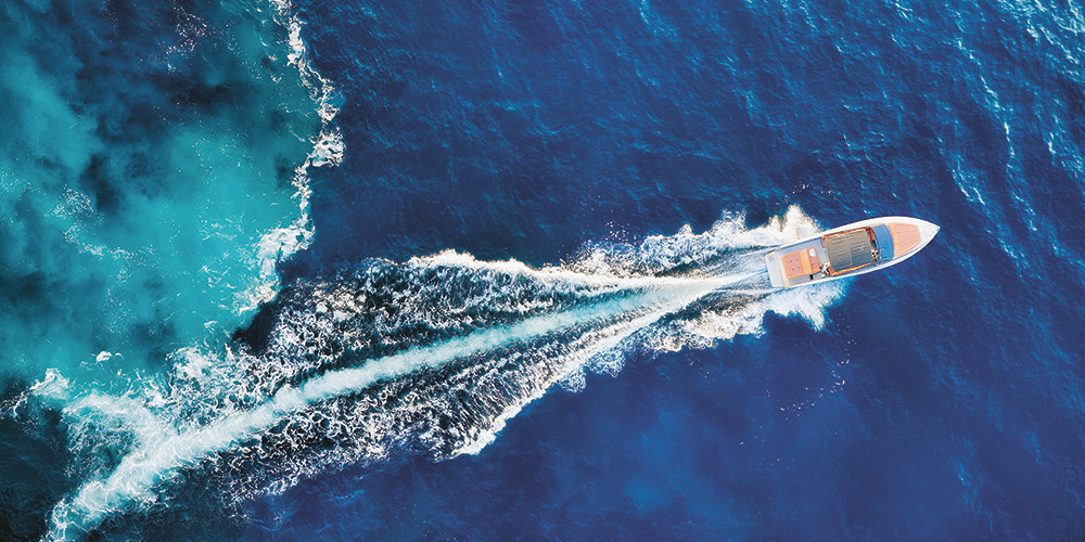 Aerial view of a motorboat speeding across the deep blue sea, leaving a wide trail of white foam behind it. Aerial view of a motorboat speeding across the deep blue sea, leaving a wide trail of white foam behind it.