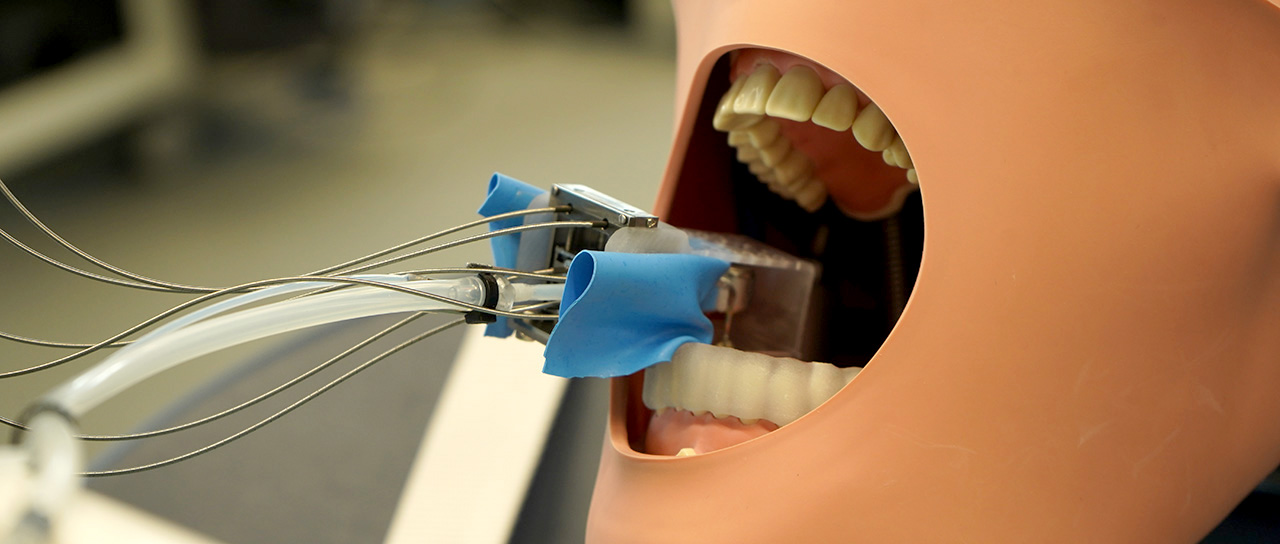A miniature robot the size of a wine cork is mounted on the teeth of a model patient made of plastic