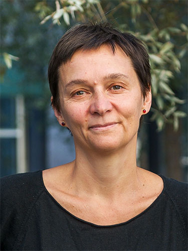 Porträt einer Frau mit kurzen dunklen Haaren und schwarzen Ohrringen, vor einem verschwommenen Hintergrund mit grünen Pflanzen. Porträt einer Frau mit kurzen dunklen Haaren und schwarzen Ohrringen, vor einem verschwommenen Hintergrund mit grünen Pflanzen.