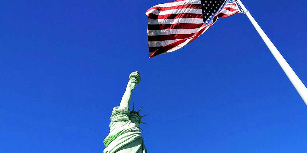 Statue of Liberty in front of the U.S. flag under a blue sky Statue of Liberty in front of the U.S. flag under a blue sky