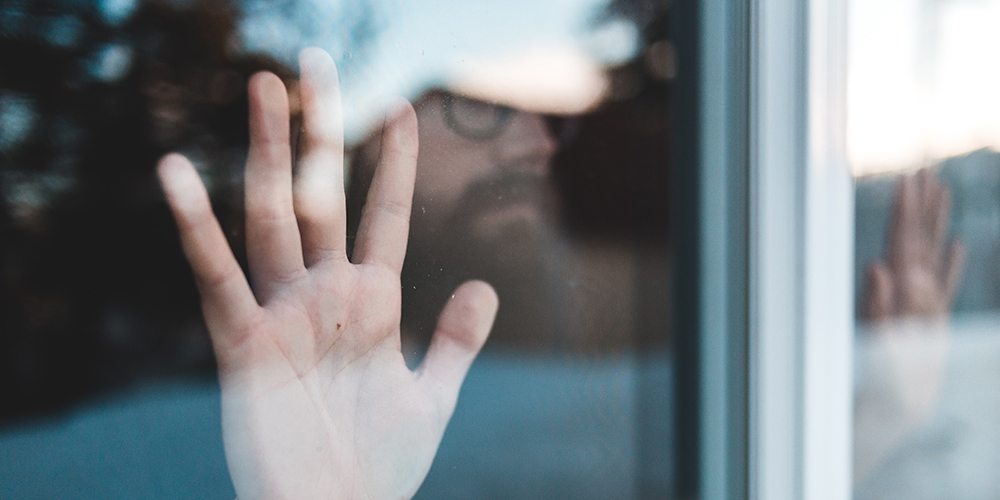 Un homme pose ses mains sur une vitre de fenêtre et regarde dehors