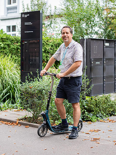 Adam Hearn steht auf seinem Trotinett vor dem Eingang eines Bürogebäudes. Adam Hearn steht auf seinem Trotinett vor dem Eingang eines Bürogebäudes.