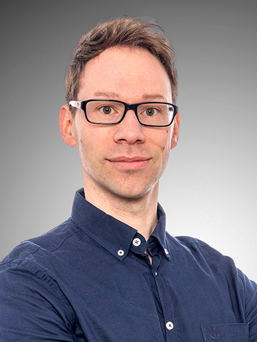 Ein Porträt eines Mannes mit kurzem braunem Haar, schwarzer Brille und dunkelblauem Hemd. Ein Porträt eines Mannes mit kurzem braunem Haar, schwarzer Brille und dunkelblauem Hemd.