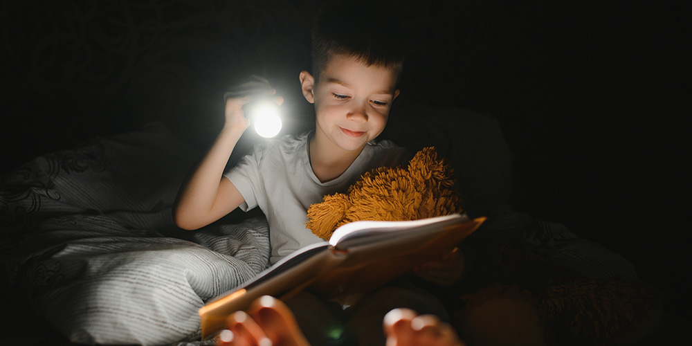 Boy reading a book with a flashlight