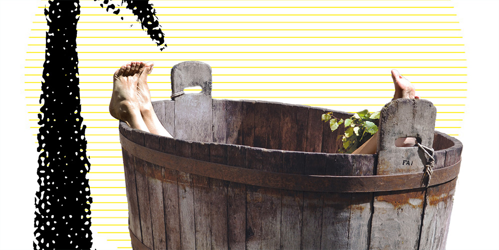 A person in a large wooden tub; only their legs and feet are sticking out over the edge. A person in a large wooden tub; only their legs and feet are sticking out over the edge.