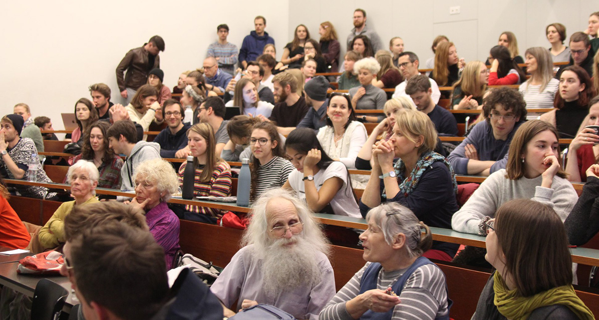 In a packed lecture hall, interested visitors to an event talk to each other.