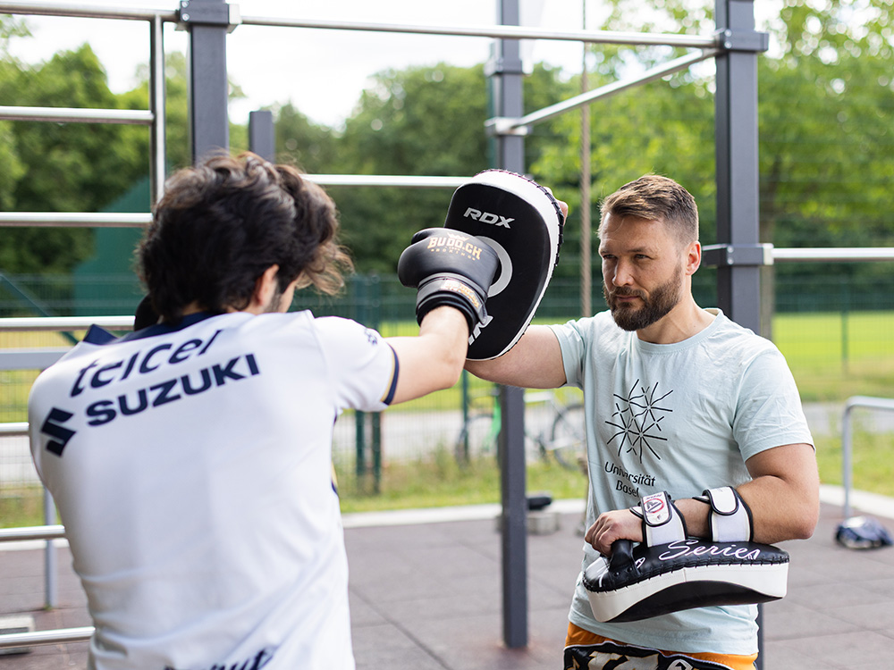 Florian Knappe and another young man are working out with boxing pads at an outdoor fitness facility. Florian Knappe and another young man are working out with boxing pads at an outdoor fitness facility.
