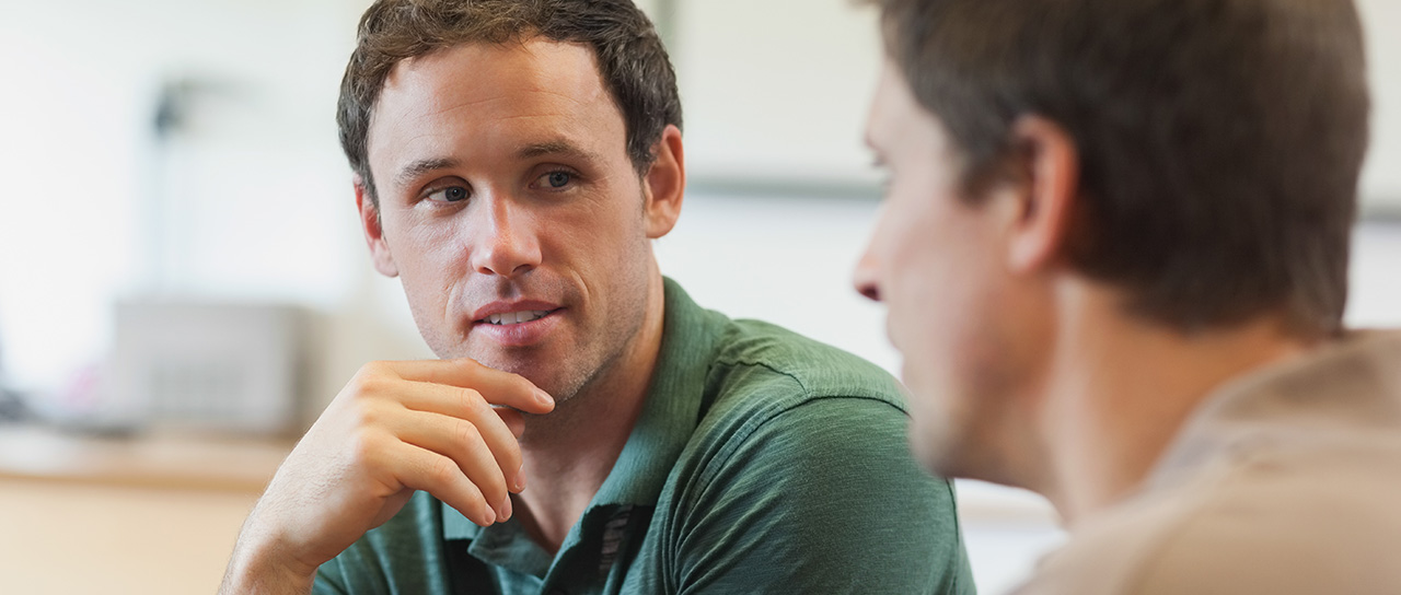 Two men engaged in a serious conversation, one facing the camera and the other seen from behind.