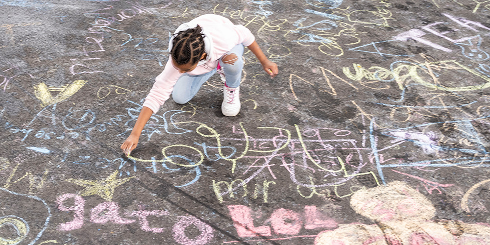 Ein Kind schreibt mit Strassenkreide aufs Trottoir. 