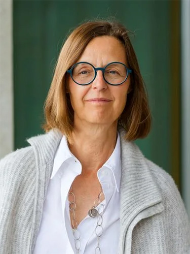 Porträt einer Frau mit kurzem braunem Haar und runder Brille, gekleidet in eine weiße Bluse und eine helle Strickjacke, vor einem modernen Gebäude. Porträt einer Frau mit kurzem braunem Haar und runder Brille, gekleidet in eine weiße Bluse und eine helle Strickjacke, vor einem modernen Gebäude.