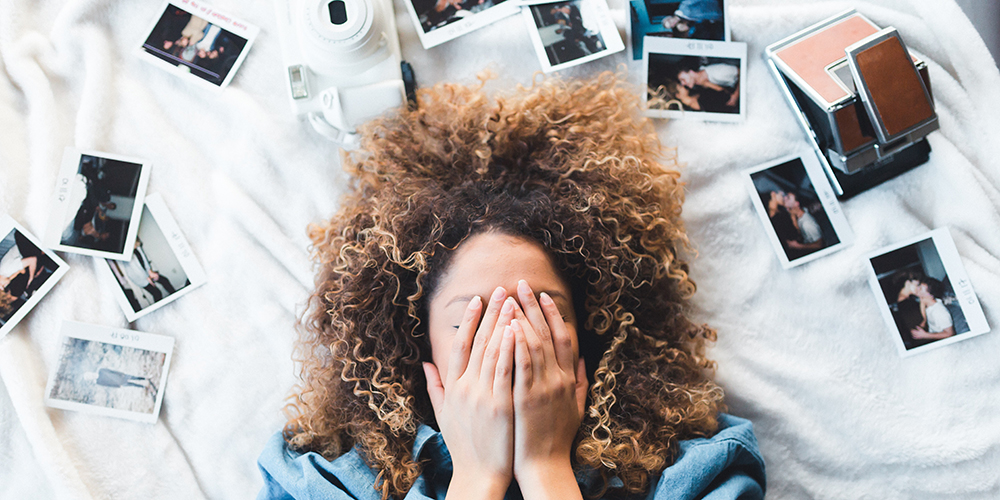 woman lying on bed covering her face, surrounded by photos