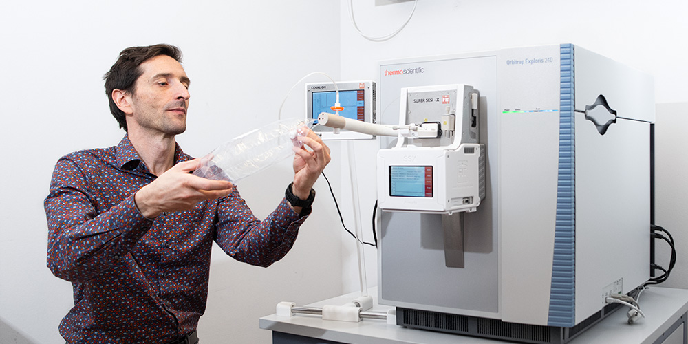 Pablo Sinues mit einem durchsichtigen Plastikbeutel mit Atemluft vor einem Massenspektrometer Pablo Sinues mit einem durchsichtigen Plastikbeutel mit Atemluft vor einem Massenspektrometer
