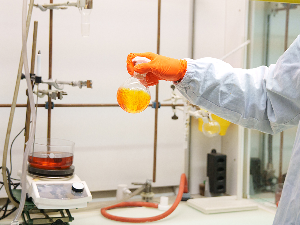 Eine orange Flüssigkeit wird von einem Chemiestudenten im Labor in die Luft gehalten. Eine orange Flüssigkeit wird von einem Chemiestudenten im Labor in die Luft gehalten.