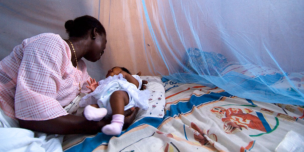 Die Mutter legt ein Kind in ein Bett, das von einem Malaria-Schutznetz umgeben ist.
