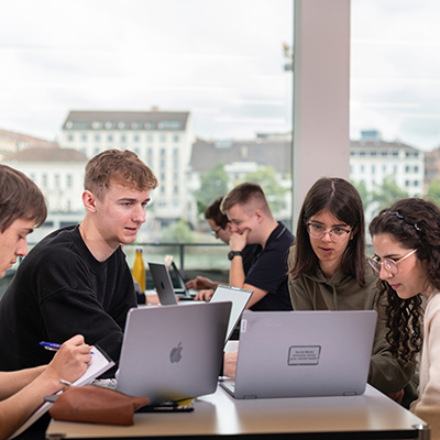 Vier Studierende sitzen um einen Tisch und bearbeiten gemeinsam eine Aufgabe.