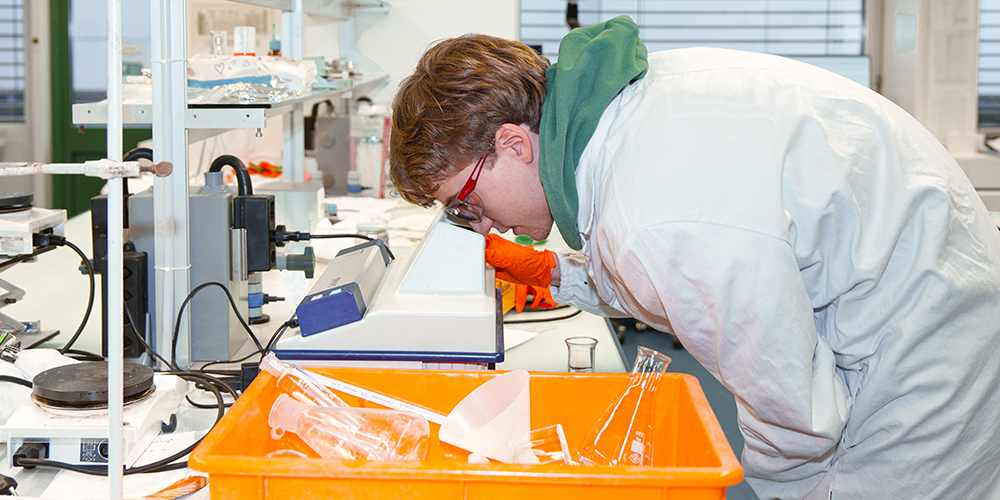 Ein Chemiestudent schaut in ein Mikroskop.